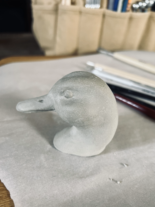 Left profile view of a clay sculpture that portrays the head of a mallard duck