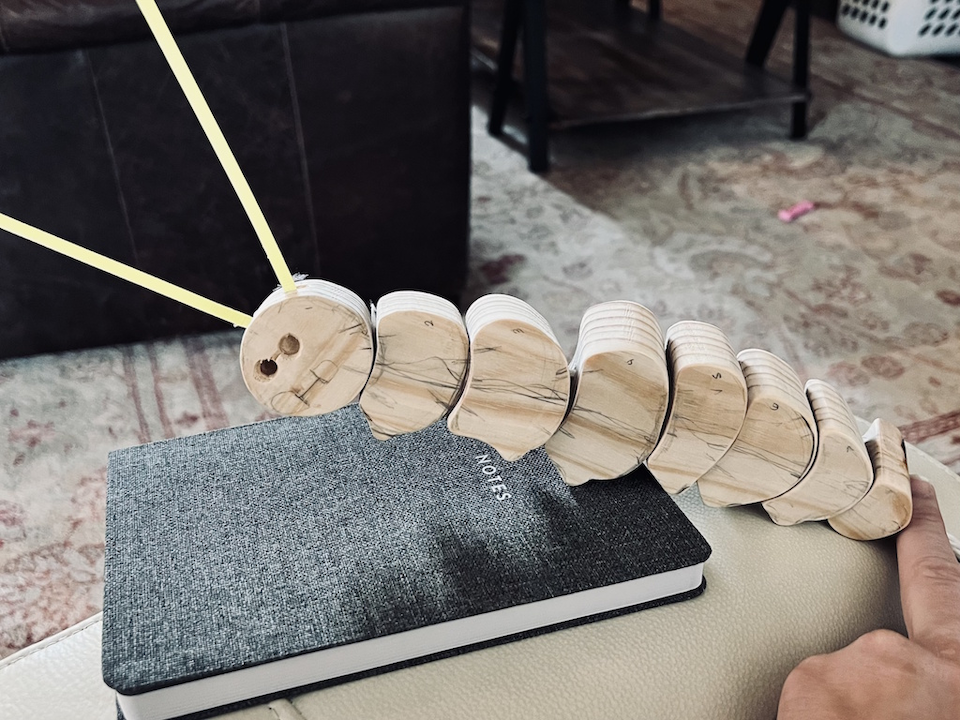 Handmade segmented wooden caterpillar toy with yellow antennae resting on a notebook.
