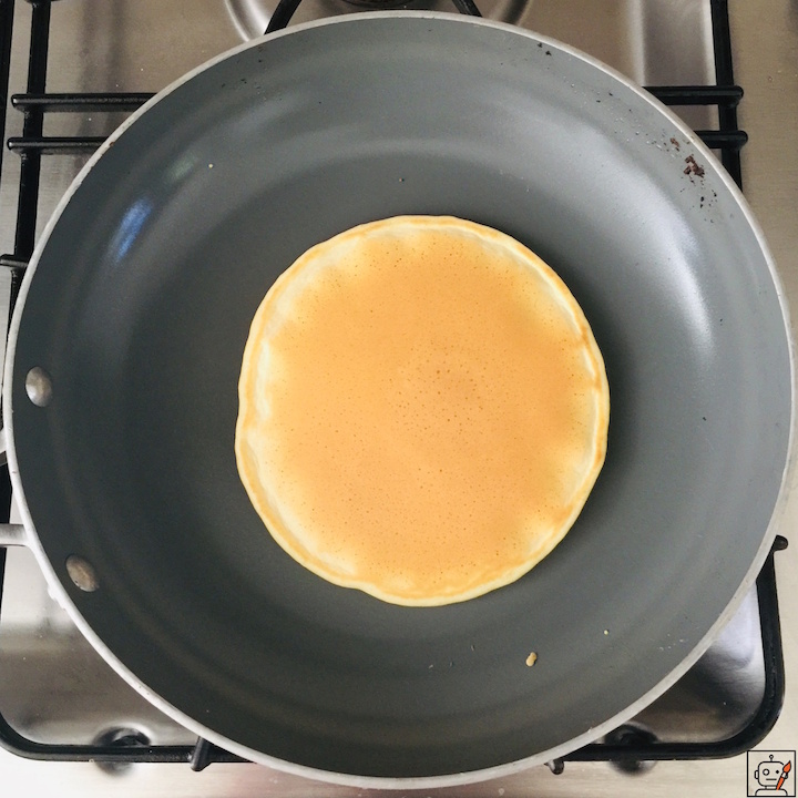 A mouth watering perfect pancake, evenly cooked in a nonstick pan, centered on a stovetop.